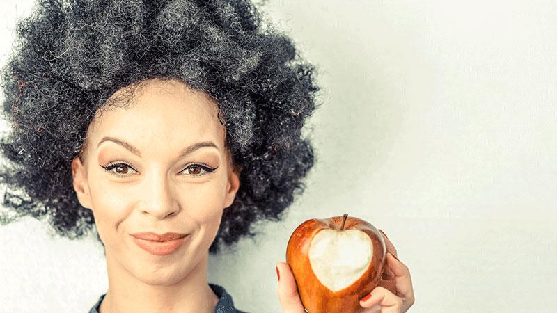 gray-haired woman eating apple with heart shape bite